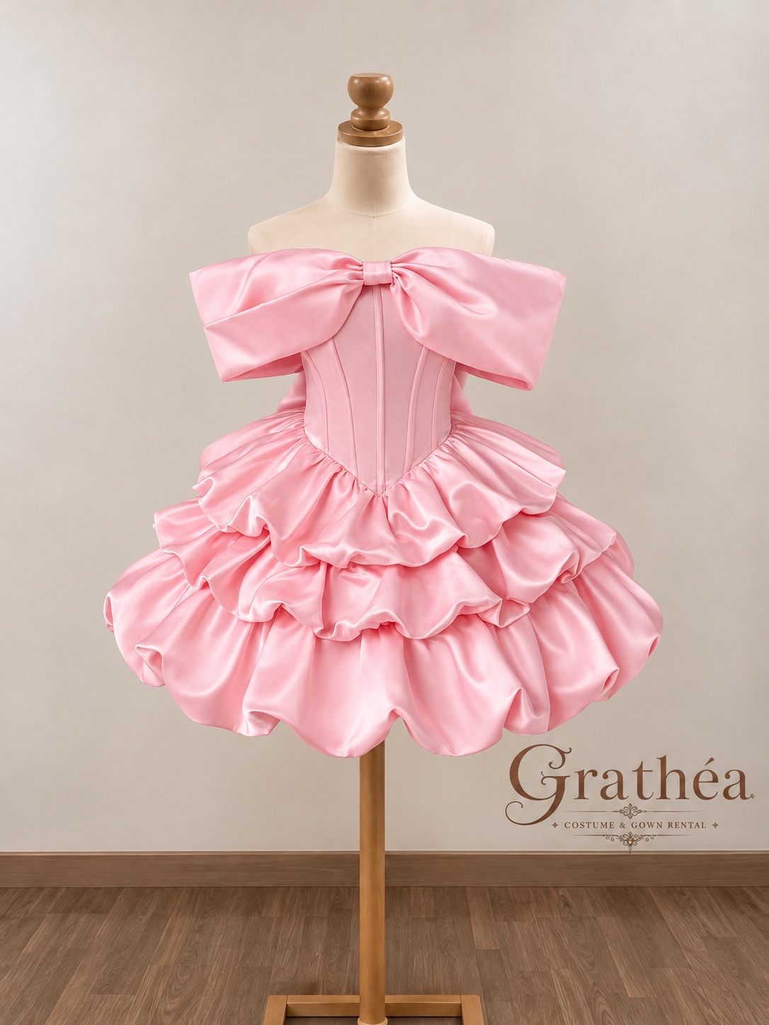Elise Pink: A soft pink cocktail dress featuring an oversized bow neckline, a structured corset-style bodice, and a pointed waist. Its lustrous satin finish and voluminous tiers of ruffles create a playful, doll-inspired silhouette, finished with a charming bubble hem. Sweet, feminine, and made to stand out. 🎀