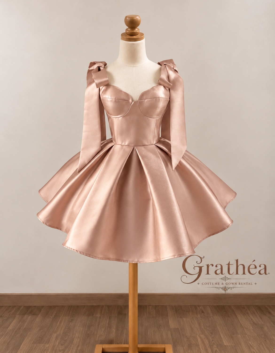 Isla: A champagne cocktail dress featuring a lustrous satin finish, a structured sweetheart bodice, and statement shoulder bows with long ribbon tails. Its fitted waist and full, pleated skirt create a romantic, feminine silhouette with timeless elegance. ✨